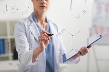 Keçeli kalemle cam tahtaya kimyasal formüller yazan bulanık doktor görüntüsü.