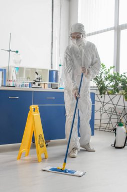 Tehlikeli madde giysisi giyen doktor laboratuarda paspasla yerleri temizliyor.