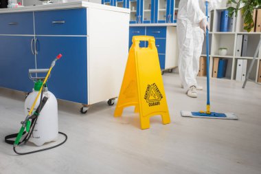 Koruyucu giysili bir bilim adamının laboratuarın zeminini temizlerken çekilmiş görüntüsü.
