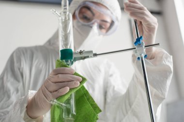 Laboratuvarda lateks eldivenli bulanık bilim adamı tripodu şişeyle temizliyor.