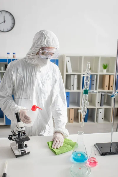 实验室靠近瓶子和显微镜的危险垫擦拭台的科学家 — 图库照片