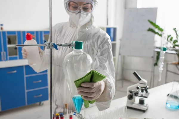穿危险物品套装的科学家在实验室消毒时用抹布擦拭瓶 — 图库照片