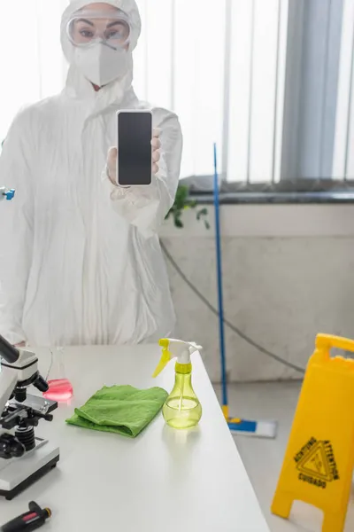 身穿防护服和护目镜的科学家在实验室展示带有空白屏幕的智能手机 — 图库照片