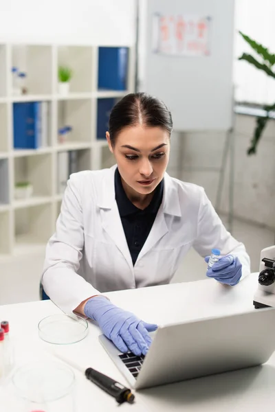 Cientista Morena Segurando Vacina Enquanto Digita Laptop Perto Placa Petri — Fotografia de Stock