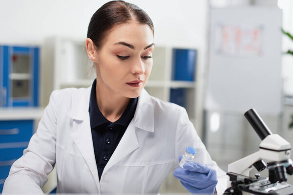 brunette scientist in white coat holding coronavirus vaccine in laboratory