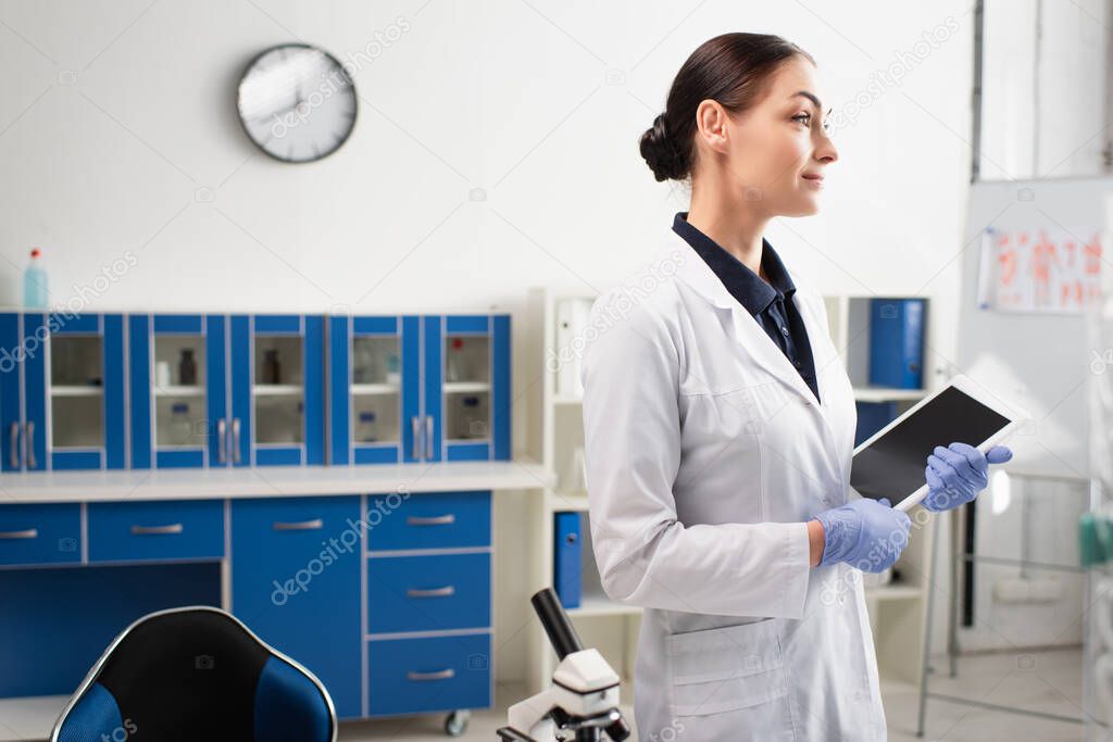 Scientist holding digital tablet with blank screen near microscope in lab 