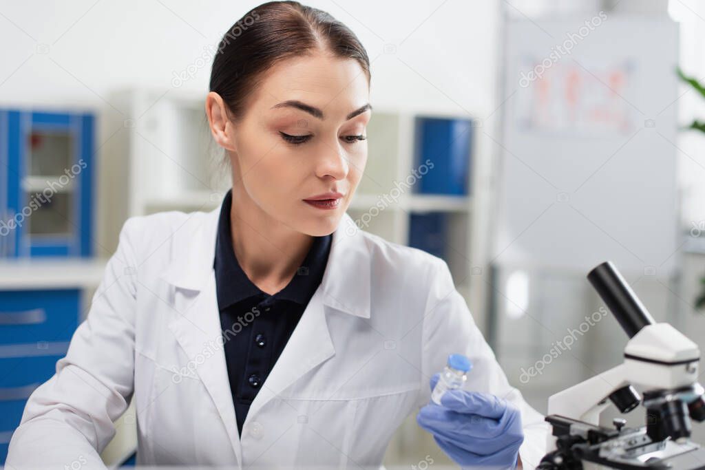 brunette scientist in white coat holding coronavirus vaccine in laboratory