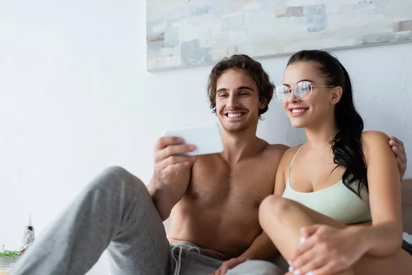 Smiling Shirtless Man Holding Blurred Smartphone Smiling Girlfriend Eyeglasses Bedroom — Stock Photo, Image