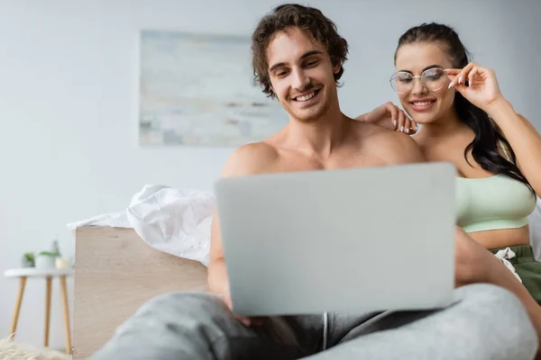 Smiling Sexy Woman Eyeglasses Looking Blurred Laptop Shirtless Boyfriend Bedroom — Stock Photo, Image