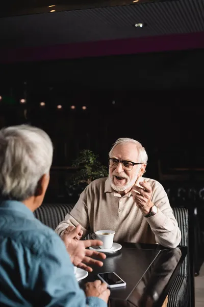 Старший Чоловік Окулярах Жестикулює Розмовляючи Розмитим Другом Кафе — стокове фото