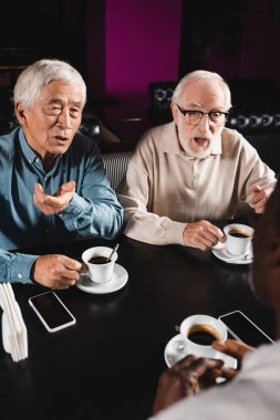 Kafe 'de Afrikalı Amerikalı bulanık bir arkadaşla konuşurken el kol hareketi yapan kıdemli ırklar arası adamlar.