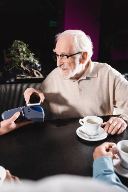 Gözlüklü adam bardaki terminalden cep telefonuyla ödeme yapıyor.