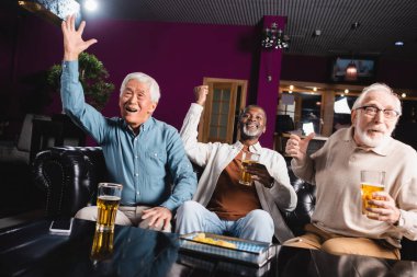 Pub 'da futbol şampiyonası izleyen ve zafer jesti yapan neşeli üst düzey etnik arkadaşlar.
