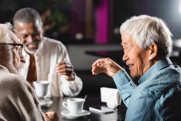 Neşeli üst düzey çok ırklı arkadaşlar kafede birlikte vakit geçiriyorlar.