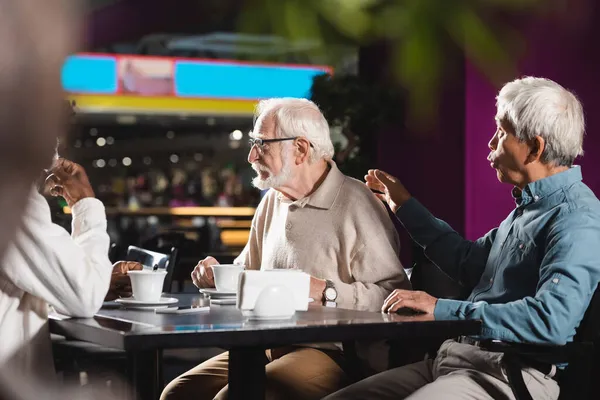 Asyalı adam, Kafe 'deki bulanık Afrikalı Amerikalı adamın yanına, kıdemli arkadaşının sırtına dokunuyor.