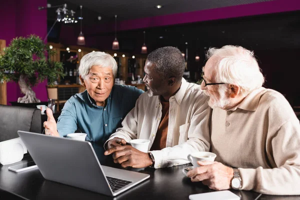 Mayores Amigos Interracial Apuntando Computadora Portátil Mientras Habla Cafetería — Foto de Stock
