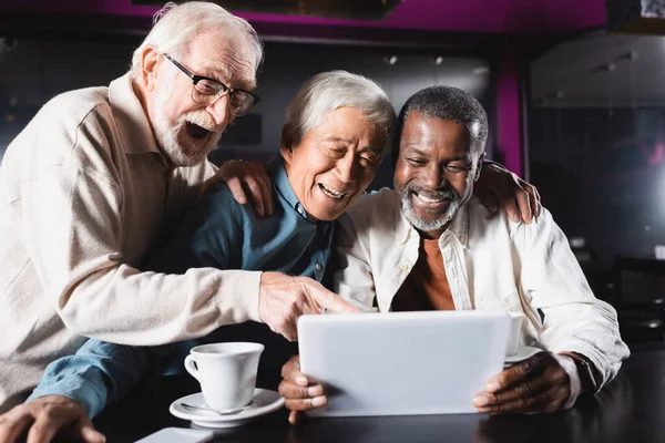 Изумленный Пожилой Человек Указывающий Цифровой Планшет Рядом Веселыми Многонациональными Друзьями — стоковое фото