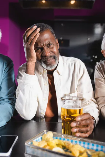 在体育酒吧观看锦标赛时 拿着一杯啤酒碰头的令人沮丧的非洲裔美国人 — 图库照片