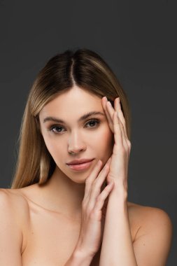 Çıplak omuzlu, mükemmel ciltli ve gri renkli kameraya bakan şehvetli genç bir kadın.