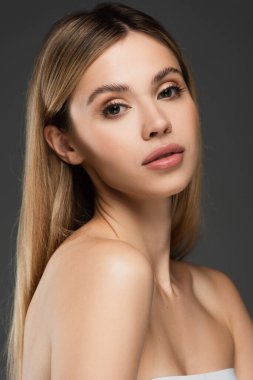 Çıplak omuzlu ve mükemmel ciltli şehvetli kadın gri renkli kameraya bakıyor.