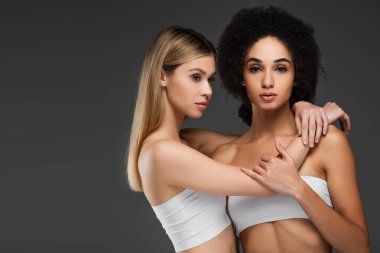 Beyaz bluzlu güzel bir kadın. Gri tenli, Afro-Amerikan kadını kucaklıyor.