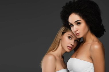 Mükemmel ciltli genç bir kadın. Afrikalı Amerikalı arkadaşına yaslanıyor. Gri üzerine izole edilmiş.