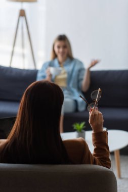 Psikoloğun elinde gözlük varken bulanık arka planda konuşan kadının arka plan görüntüsü