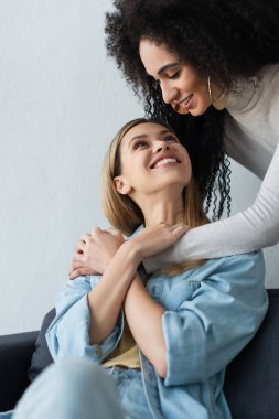 Genç, çok ırklı lezbiyen kadınlar birbirlerine gülümserken kucaklaşıyorlar.