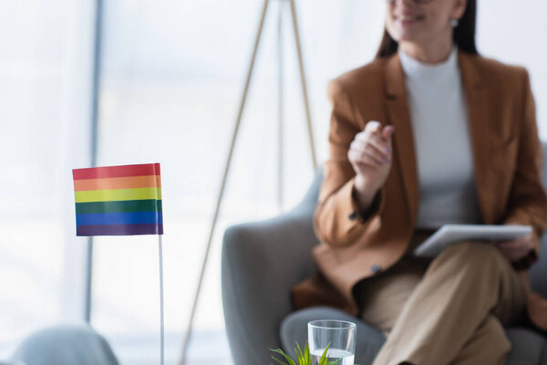 small lgbt flag near cropped psychologist with digital tablet on blurred background