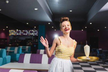 Heyecanlı genç kız garson elinde milkshake ile kafede el kol hareketi yapıyor. 