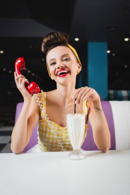 Cafe 'de milkshake masasının yanında elinde eski model bir cep telefonu tutan mutlu bir kadın.