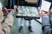 partial view of blurred business partners near man with dollars in briefcase