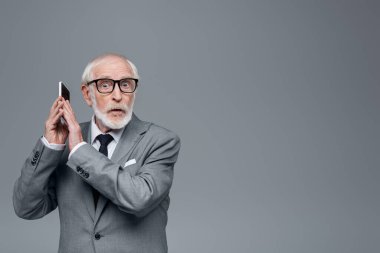Gri renkli kameraya bakarken akıllı telefonu elleriyle kapatan kıdemli işadamı şaşırdı.
