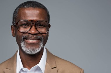 Gözlüklü Afrikalı Amerikalı iş adamı gri kameraya gülümsüyor.