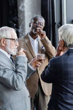 elderly successful business partners smoking cigars and drinking whiskey in office clipart