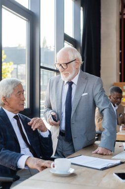 Cep telefonlu üst düzey işadamı, Asyalı meslektaşıyla masasında anlaşmalı bulanık bir şekilde konuşuyor.