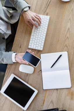 Ofiste cep telefonu tutan ve bilgisayar klavyesi kullanan işadamlarının görüntüsü. 
