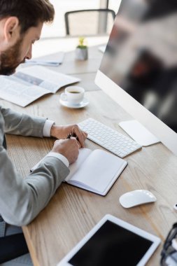 İş adamı defterine cihazların yanında yazıyor ve ofiste kahve içiyor. 