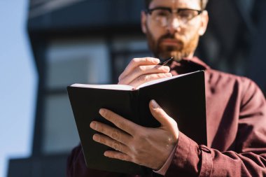Bulanık iş adamının açık havada kalem ve defter tutmasının düşük açılı görüntüsü 