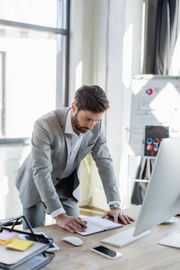 Ofisteki cihazların ve kağıtların yanındaki defterlere bakan iş adamı 