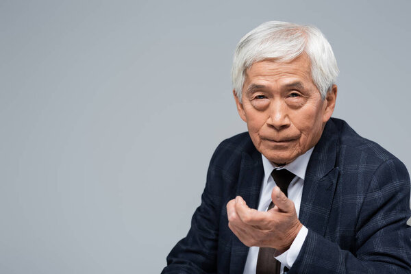 senior asian businessman with outstretched hand looking at camera isolated on grey