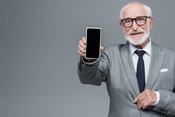 blurred senior businessman showing mobile phone with blank screen isolated on grey
