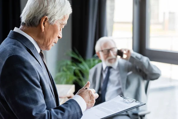 Senior Asiatischer Geschäftsmann Liest Vertrag Während Kollege Auf Smartphone Auf — Stockfoto