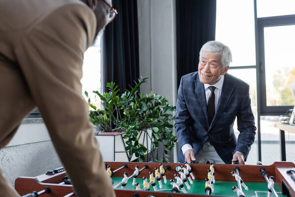 blurred african american businessman playing table football with senior asian colleague