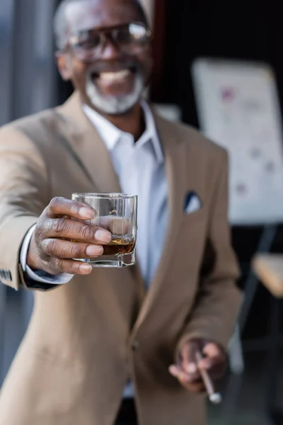 Hombre Negocios Afroamericano Borroso Sonriendo Mientras Sostiene Vaso Whisky Mano —  Fotos de Stock