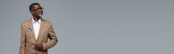 senior african american businessman in formal wear and eyeglasses looking away isolated on grey, banner