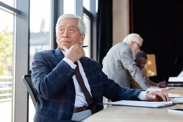 Старший Азиатский Бизнесмен Смотрит Сторону Работая Рядом Размытые Мультиэтнические Коллеги — стоковое фото
