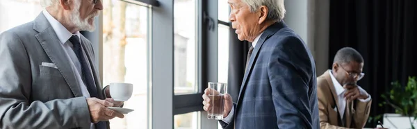 Hombres Negocios Senior Con Bebidas Hablando Mientras Colega Afroamericano Trabaja —  Fotos de Stock