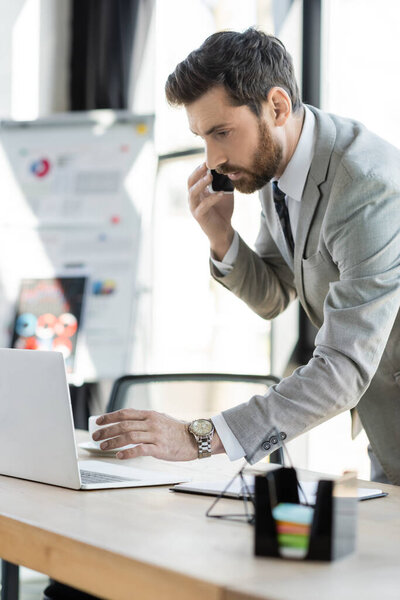 Businessman talking on smartphone near laptop in office 