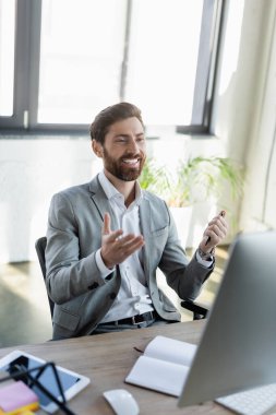 Ofisteki bilgisayarın yanındaki bilgisayarda video görüşmesi sırasında eliyle işaret eden olumlu iş adamı 